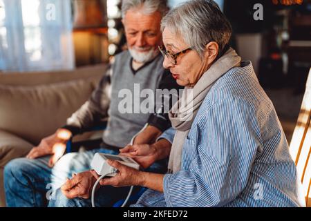 Coppia anziana a casa che misura la pressione sanguigna. Concetto di assistenza sanitaria per il monitoraggio domestico delle persone Foto Stock