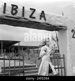 Fashion shoot sull'isola spagnola Ibiza negli anni '1960s. Un modello di moda nella moda decennale. Un cappotto bianco corto sopra un vestito. 1967 Foto Stock