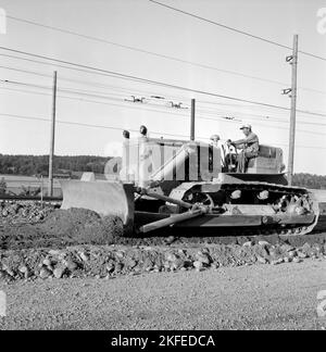 Negli anni '1950s. Il macchinario pesante, un bulldozer sembra gigantesco quando paragonato a hte uomo seduto nel sedile del conducente con cabina o protezione intorno a lui. Si tratta di un motore diesel Caterpillar da 20 tonnellate, modello D7, 240 cv. Cat è l'abbreviazione di Caterpillar. La foto viene scattata su un cantiere ferroviario quando il bulldozer appiattisce e distribuisce il materiale utilizzato per la posa dei binari ferroviari. Svezia agosto 1955 Foto Stock