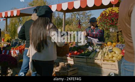 Contadino anziano con baffi boscati confezionano le banane in una borsa ecologica. L'uomo afroamericano paga fuori in contanti. Shopping multietnico presso il mercato agricolo locale. Cibo vegetariano e biologico. Agricoltura. Foto Stock