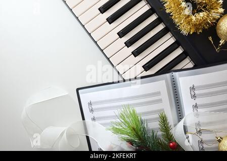 Musica corale di natale di sottofondo con pianoforte, cartella con spartiti e decorazione natalizia su tavolo bianco. Vista dall'alto. Foto Stock