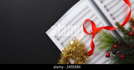 Musica corale di natale di sottofondo con musica spartiti e decorazione natalizia su tavolo nero. Vista dall'alto. Foto Stock