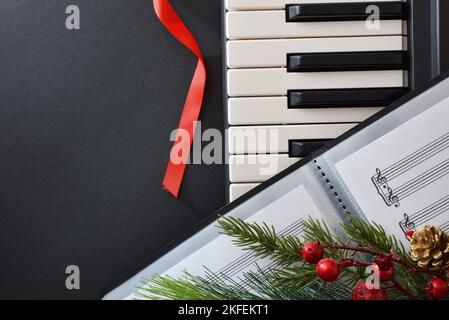 Dettaglio concettuale del concerto natalizio di coro e pianoforte con strumento e cartella con spartiti su tavola nera e decorazione natalizia. Top vie Foto Stock