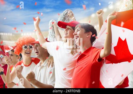 Tifoso canadese per il calcio allo stadio. Tifosi canadesi sul campo di calcio che guardano la squadra giocare. Gruppo di sostenitori con bandiera e maglia nazionale di cui rallegrarsi Foto Stock