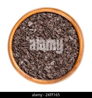 Guarnizione in scaglie di cioccolato fondente, in una ciotola di legno. Gli spruzzi di cioccolato, usati nella cottura come decorazione o per aggiungere la consistenza ai biscotti, alle torte ed ai dessert. Foto Stock