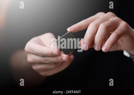 Le mani di Mans che tengono una piccola scatola nera quadrata con uno spazio vuoto della copia per il testo ed il disegno isolato su fondo scuro. Scheda, vuota, modello, mockup, Foto Stock