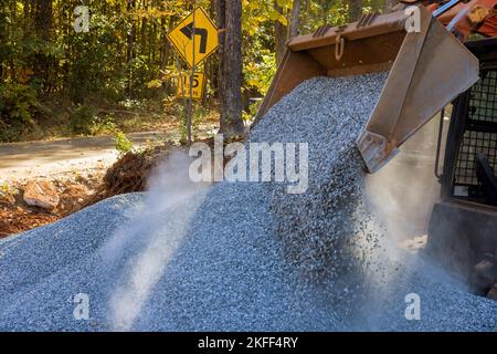 Nello scarico della pietra frantumata in cantiere durante il progetto di riparazione stradale è stato utilizzato l'escavatore con caricatore Bobcat. Foto Stock