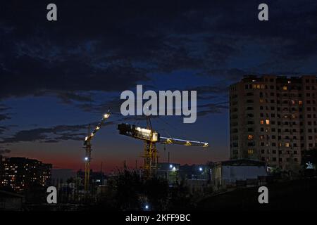 Yerevan, Armenia - 27 ottobre 2022: Gru a torre illuminate in un cantiere durante il tramonto in arancione e rosso. Foto Stock