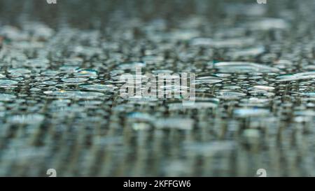 Le gocce di pioggia sulla superficie di vetro di un tavolo da giardino formano un motivo monocromatico Foto Stock