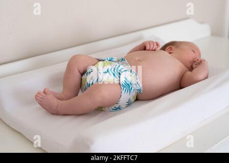 Un bambino sdraiato su un letto con la messa a fuoco sulle gambe e sul panno del bambino, pannolino riutilizzabile con una bella stampa delle foglie Foto Stock