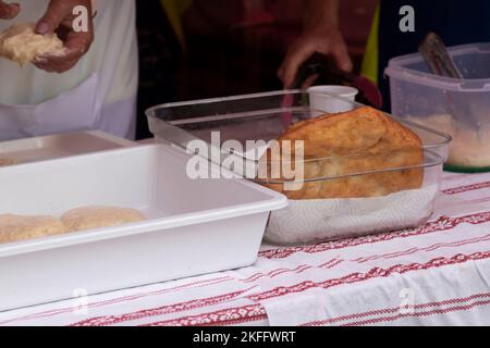 Cottura a mano femminile Lángos - un tipico cibo di strada ungherese, è un pane piatto fritto con fondo di panna acida Foto Stock