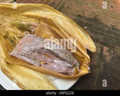 Tamale prodotto da mais blu con fiori di zucca avvolti in una buccia di mais a Oaxaca, Messico. Cibo Oaxacan fatto in casa. Foto Stock