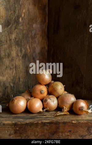 Cipolle fresche impilate su una superficie in legno in un ambiente rustico Foto Stock