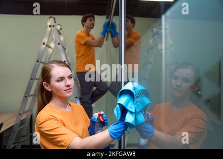 Due dipendenti delle aziende che si occupa della pulizia e della disinfezione di una superficie di vetro Foto Stock