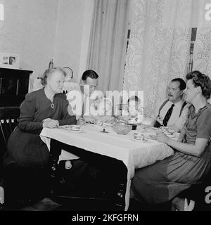 1950s, storia, vita familiare nel dopoguerra in Gran Bretagna, diverse generazioni si siedono intorno a un piccolo tavolo di legno coperto di stoffa con il tè insieme. Foto Stock