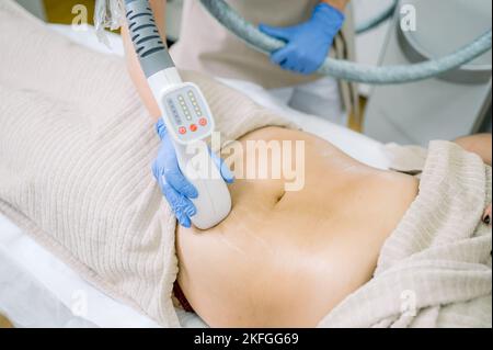 Cliente irriconoscibile e cosmetologo durante il massaggio ventre sotto vuoto Foto Stock