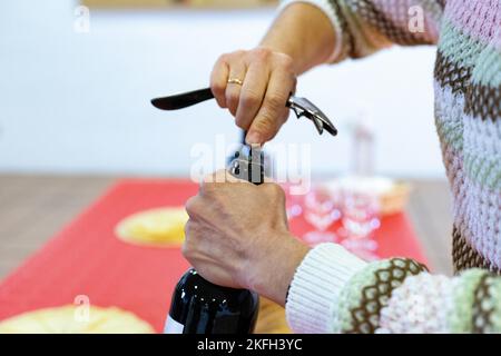 Cavatappi. È venuto. Tempo di aprire la bottiglia di vino rosso con il cavatappi. Le mani della donna che tiene la bottiglia mentre apre il sughero. Foto orizzontale Foto Stock