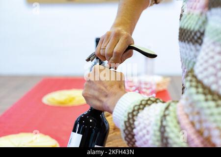 Cavatappi. È venuto. Tempo di aprire la bottiglia di vino rosso con il cavatappi. Le mani della donna che tiene la bottiglia mentre apre il sughero. Foto orizzontale Foto Stock