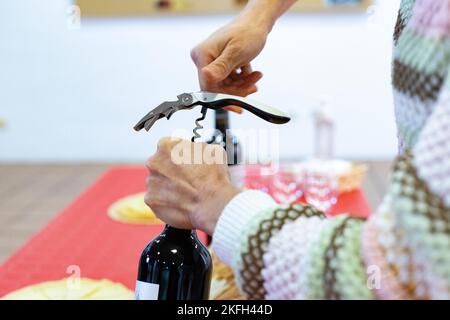 Cavatappi. È venuto. Tempo di aprire la bottiglia di vino rosso con il cavatappi. Le mani della donna che tiene la bottiglia mentre apre il sughero. Foto orizzontale Foto Stock