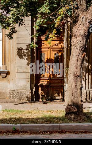 Chiuso porta di legno di una casa durante il giorno. Vibe autunnale, foglie appassite sul marciapiede, l'ombra di un albero cade sulla porta. Foto Stock