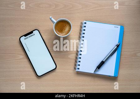 Telefono cellulare con 2023 obiettivi testo per implementare le risoluzioni di Capodanno e pianificare sulla scrivania con un bar e un diario Foto Stock