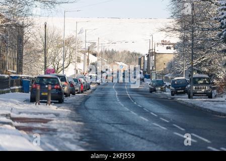 Strada asfaltata con neve sui sentieri. Neve sulle colline sullo sfondo. Auto parcheggiate sul lato della strada. Prendi Burnley Road, Loveclough Foto Stock