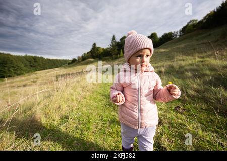 Ragazza carina cucciolata che cammina sulla collina autunnale indossando una giacca rosa e stivali di gomma. Foto Stock
