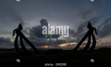 Incredibile tramonto con splendide nuvole grigie nel cielo. Scultura a mezza luna a Heysham con uomini di metallo seduti sulla struttura che si affaccia sul mare. Foto Stock