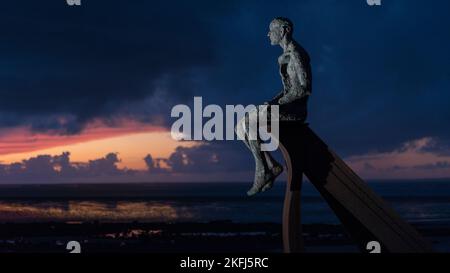 Incredibile tramonto con splendide nuvole grigie nel cielo. Scultura a mezza luna a Heysham con uomini di metallo seduti sulla struttura che si affaccia sul mare. Foto Stock