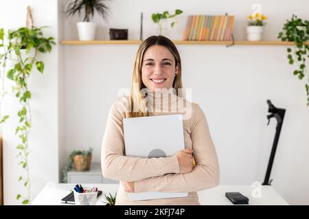 Giovane donna d'affari sorridente e di successo che tiene in mano un tablet digitale in ufficio Foto Stock