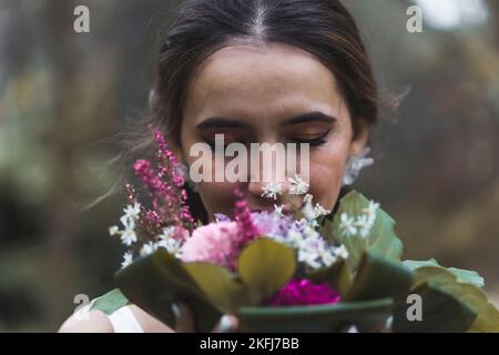 Primo piano ritratto della bella sposa mediorientale dai capelli castani odorando i fiori colorati del suo bouquet nuziale. Sfondo sfocato. Foto all'aperto appena sposata. Foto di alta qualità Foto Stock