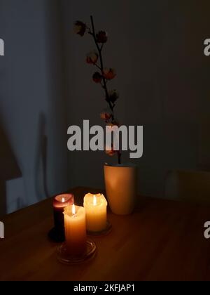 Tre candele che si illuminano su un tavolo di legno con ramo di pianta di cotone in vaso bianco sullo sfondo Foto Stock