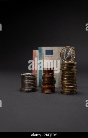 Una moneta in euro su sfondo scuro. Concetto di monete in euro impilate con banconote in euro dietro e fuori fuoco. Spazio di copia. Foto Stock