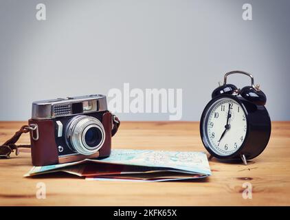 Alzati e risplendi il tempo per andare alla scoperta. Una macchina fotografica e una mappa sdraiati sul tavolo accanto a una sveglia. Foto Stock