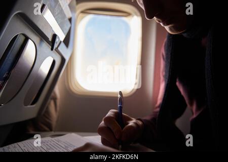 Mano turistica compilando il modulo di immigrazione sul volo per visitare il paese di destinazione seduto in aereo. L'uomo sta scrivendo il permesso di ingresso o il visto su un foglio su un Foto Stock