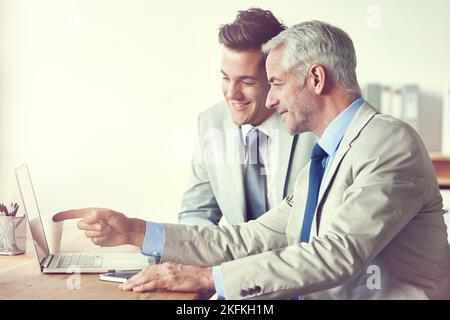 Confronto di note. Due uomini d'affari che lavorano insieme su un portatile in un ufficio. Foto Stock