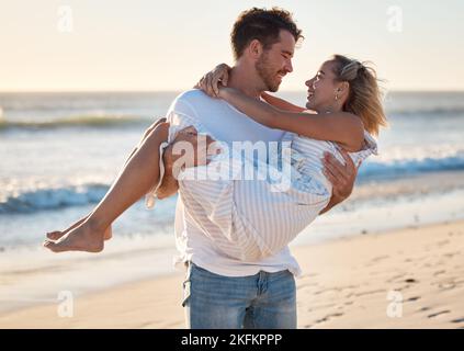 Coppia, spiaggia e uomo che porta donna per amore, relax e sostegno matrimoniale insieme in viaggio avventura o vacanza. Libertà, fiducia e uomo felice a. Foto Stock