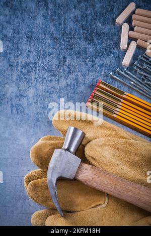 Vista ravvicinata dei guanti di protezione in pelle con martello da artiglio in legno misura in acciaio chiodi e tasselli su fondo metallico graffiato concetto di costruzione. Foto Stock