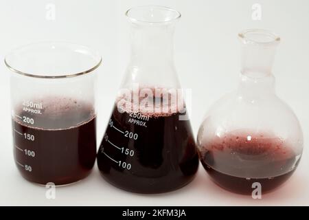 Set da laboratorio di vetreria di matracci conici, bollenti e volumetrici che contiene liquido rosso scuro con bolle dopo un esperimento scientifico Foto Stock