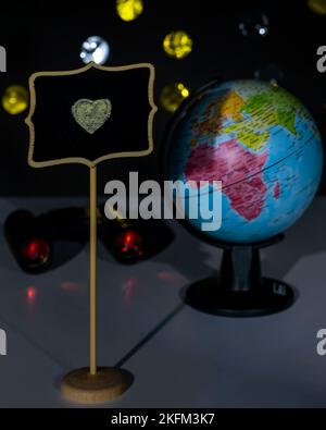 Un cuore giallo è disegnato in gesso su una piccola lavagna con un globo e binocolo sullo sfondo Foto Stock