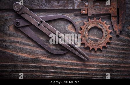 Pinze di misurazione obsolete e arrugginite con ruota dentata su un concetto di costruzione di superfici in legno scuro vintage. Foto Stock