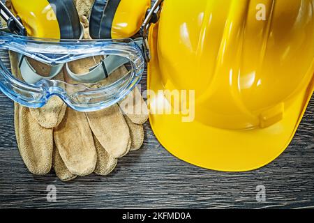 Guanti di sicurezza occhiali di protezione cuffie elmetto su asse di legno. Foto Stock