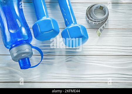 Set di tape misura bottiglia d'acqua blu manubri-campane su tavola di legno concetto di fitness. Foto Stock