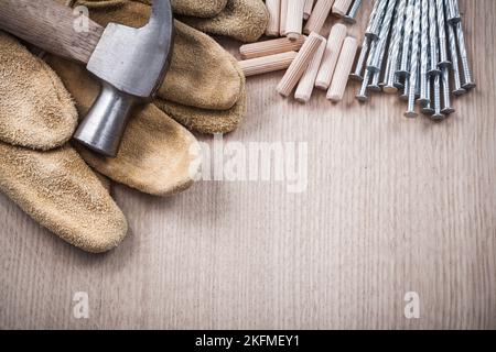 Pila di tasselli in legno martello a artiglio guanti da lavoro in pelle e chiodi in acciaio inossidabile su asse di legno Vista ravvicinata costruzione concetto. Foto Stock