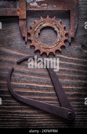 Vista dall'alto delle pinze di misurazione di lunga durata con ruota dentata su un concetto di costruzione di superfici in legno scuro vintage. Foto Stock