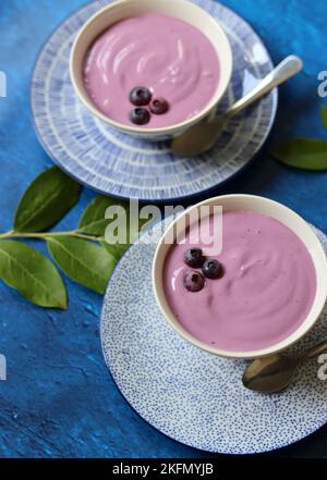 Due ciotole di yogurt al mirtillo su un tavolo. Foto ravvicinata di yogurt naturale con bacche biologiche. Mangiare concetto fresco. Foto Stock