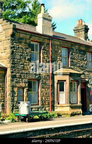 Luce del sole sulla casa della stazione e biglietteria a Goathland, North Yorkshire Moors Railway, con briciole di latte su un trolley piattaforma. Foto Stock