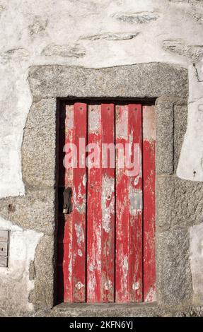 Antica porta rossa. Porta di legno intemperiato di casa rurale. Edificio in pietra con porte in legno chiuse. Concetto di minimalismo. Architettura medievale. Foto Stock