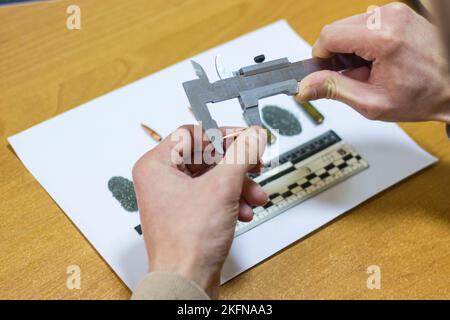 Le mani degli uomini con un calibro misurano un proiettile Foto Stock