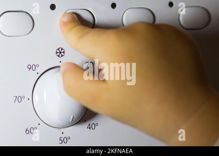 La mano di un bambino preme un pulsante su una lavatrice Foto Stock